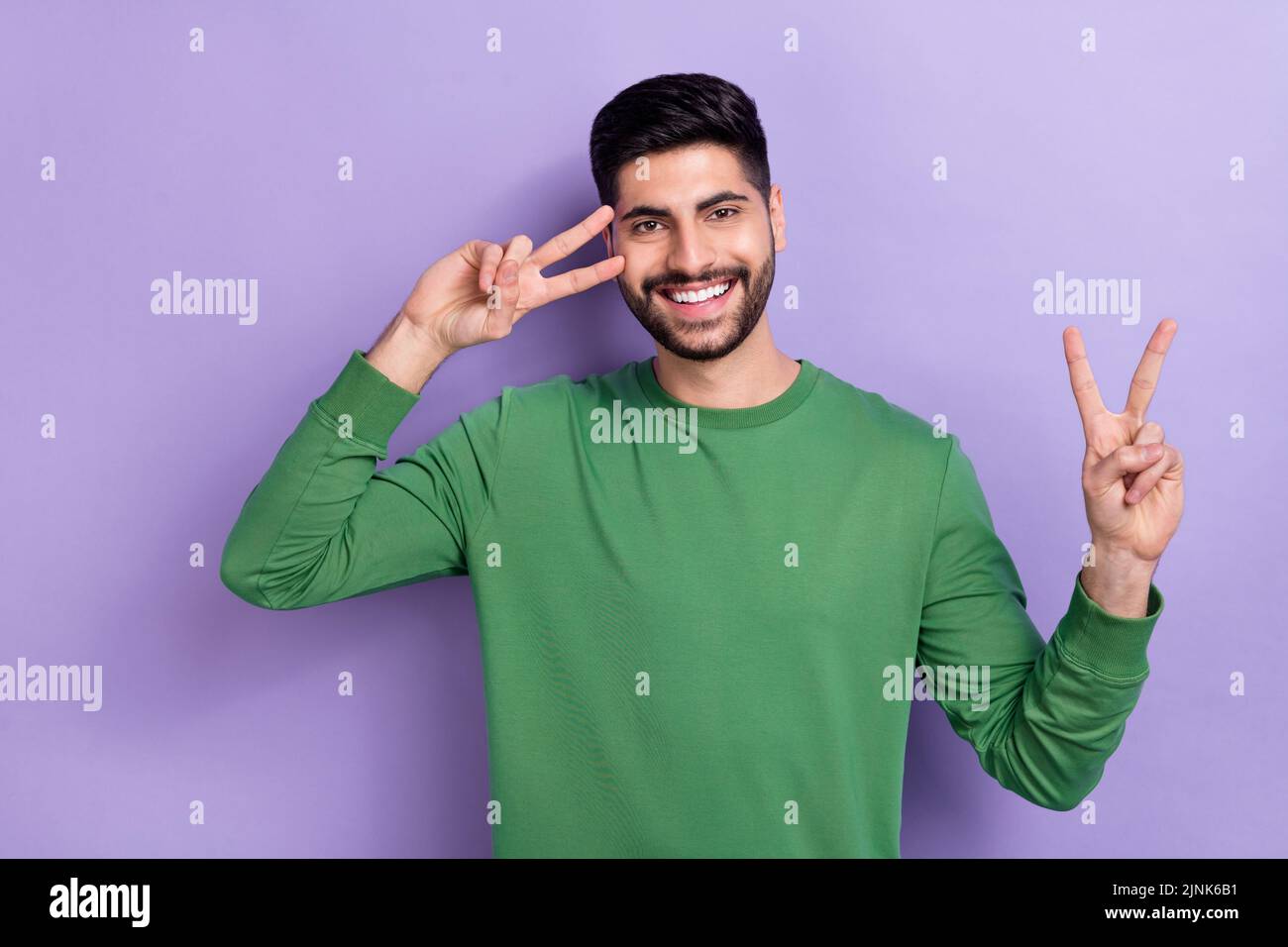Photo d'une belle personne de bonne humeur vêtue de pull vert montrant le V-signe près de la joue d'oeil isolé souriant sur fond violet de couleur Banque D'Images