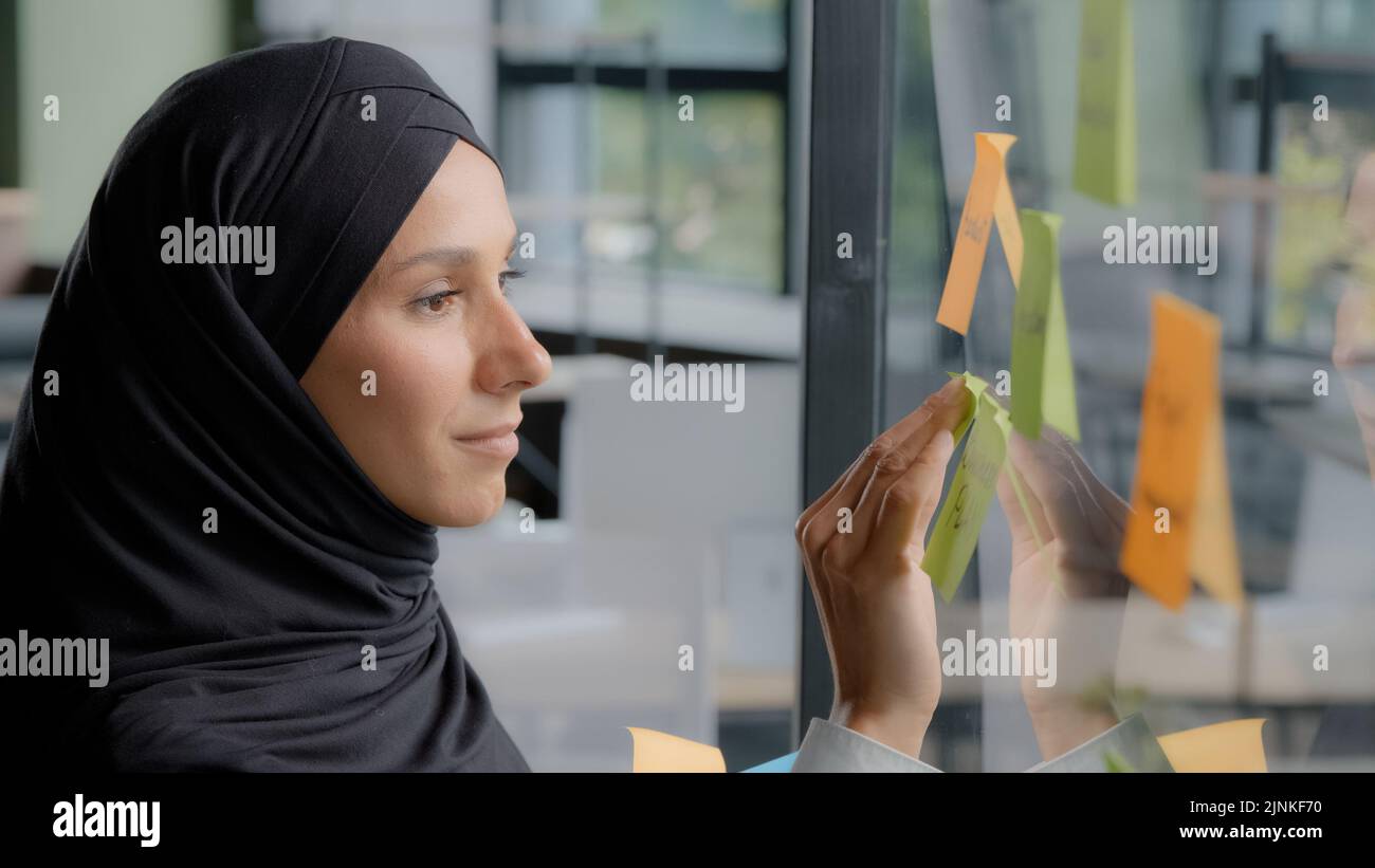 Souriante femme d'affaires réussie chef d'entreprise écrivant des tâches de projet laisse un rappel sur la note colorée collante organise le travail jeune femme arabe bureau Banque D'Images