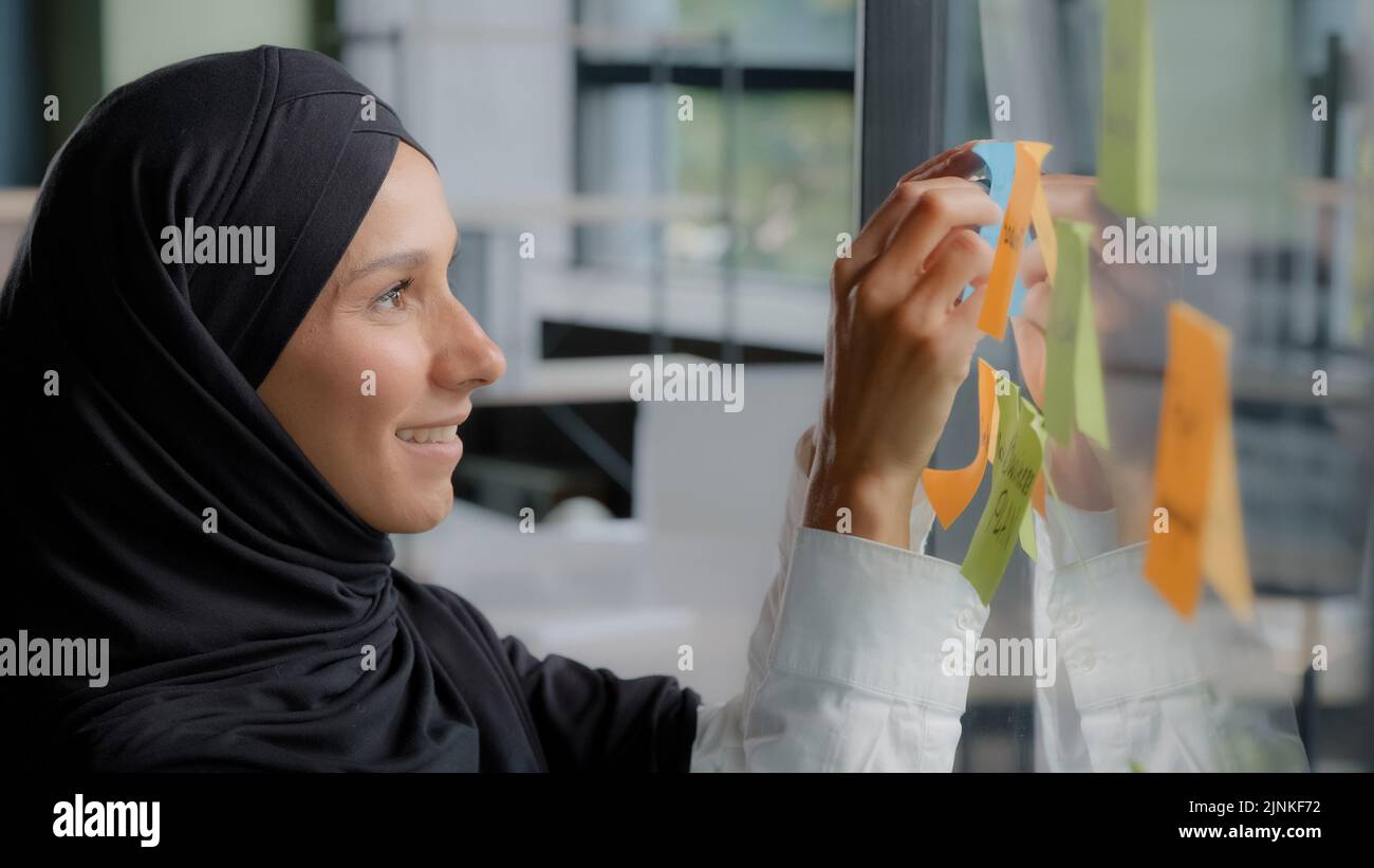 Souriante femme d'affaires réussie chef d'entreprise écrivant des tâches de projet laisse un rappel sur la note colorée collante organise le travail jeune femme arabe bureau Banque D'Images
