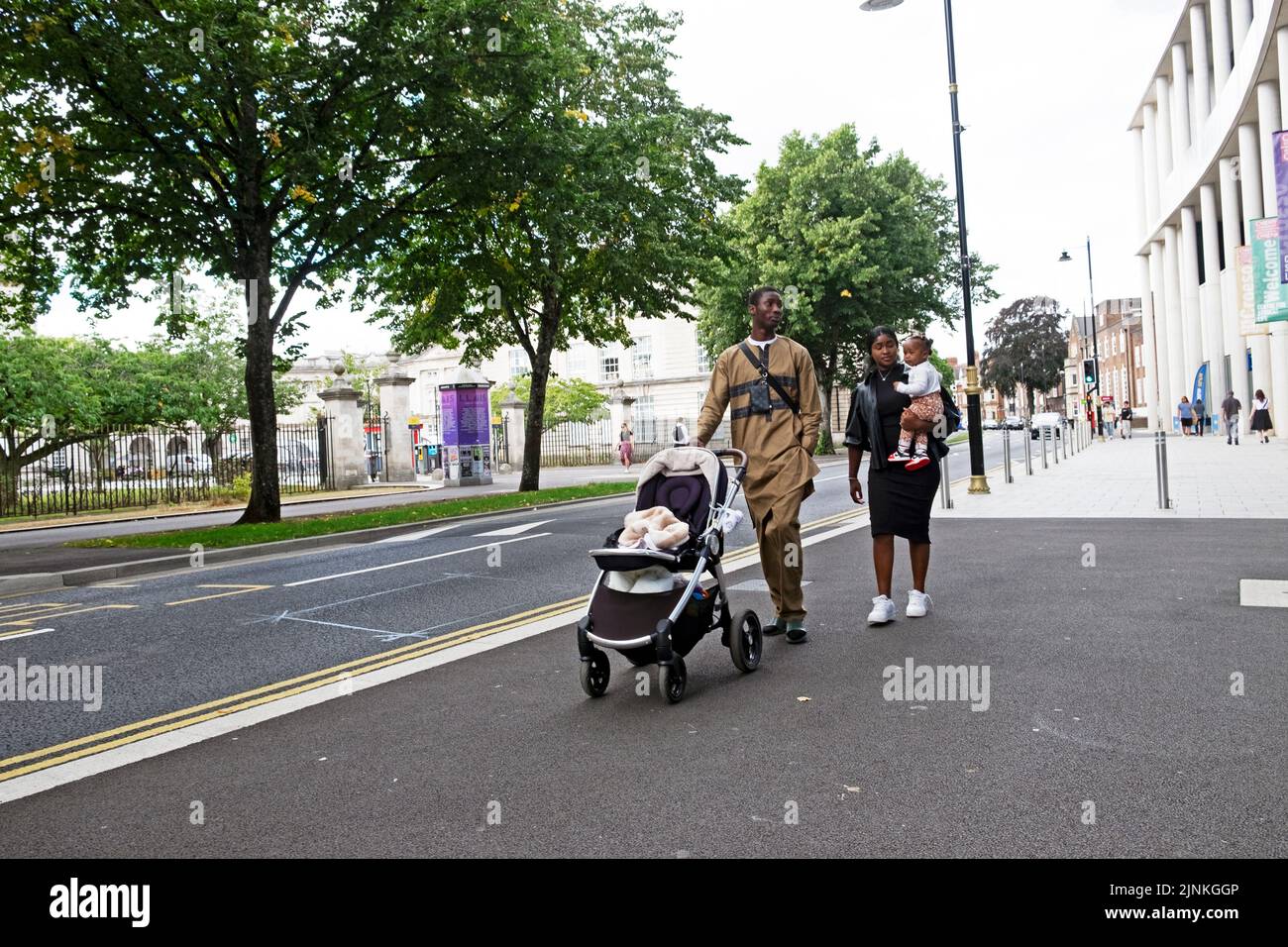 Famille noire avec maman transportant un enfant père poussant poussette poussette poussette marche dans la rue à l'extérieur de l'université de Cardiff bâtiment pays de Galles Royaume-Uni KATHY DEWITT Banque D'Images