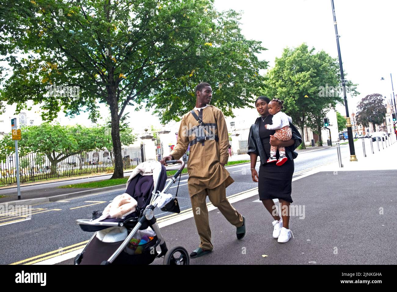 Famille noire avec maman transportant un enfant père poussant poussette poussette poussette marche dans la rue à l'extérieur de l'université de Cardiff bâtiment pays de Galles Royaume-Uni KATHY DEWITT Banque D'Images