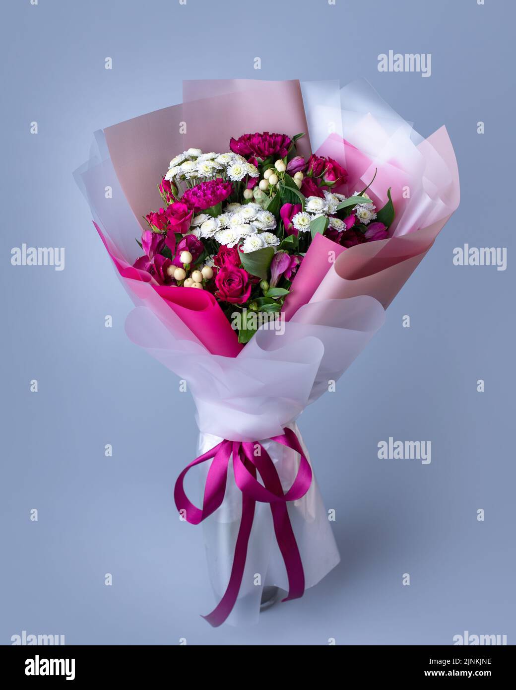 Bouquet de fleurs roses et blanches enveloppées de papier floral sur fond bleu. Banque D'Images