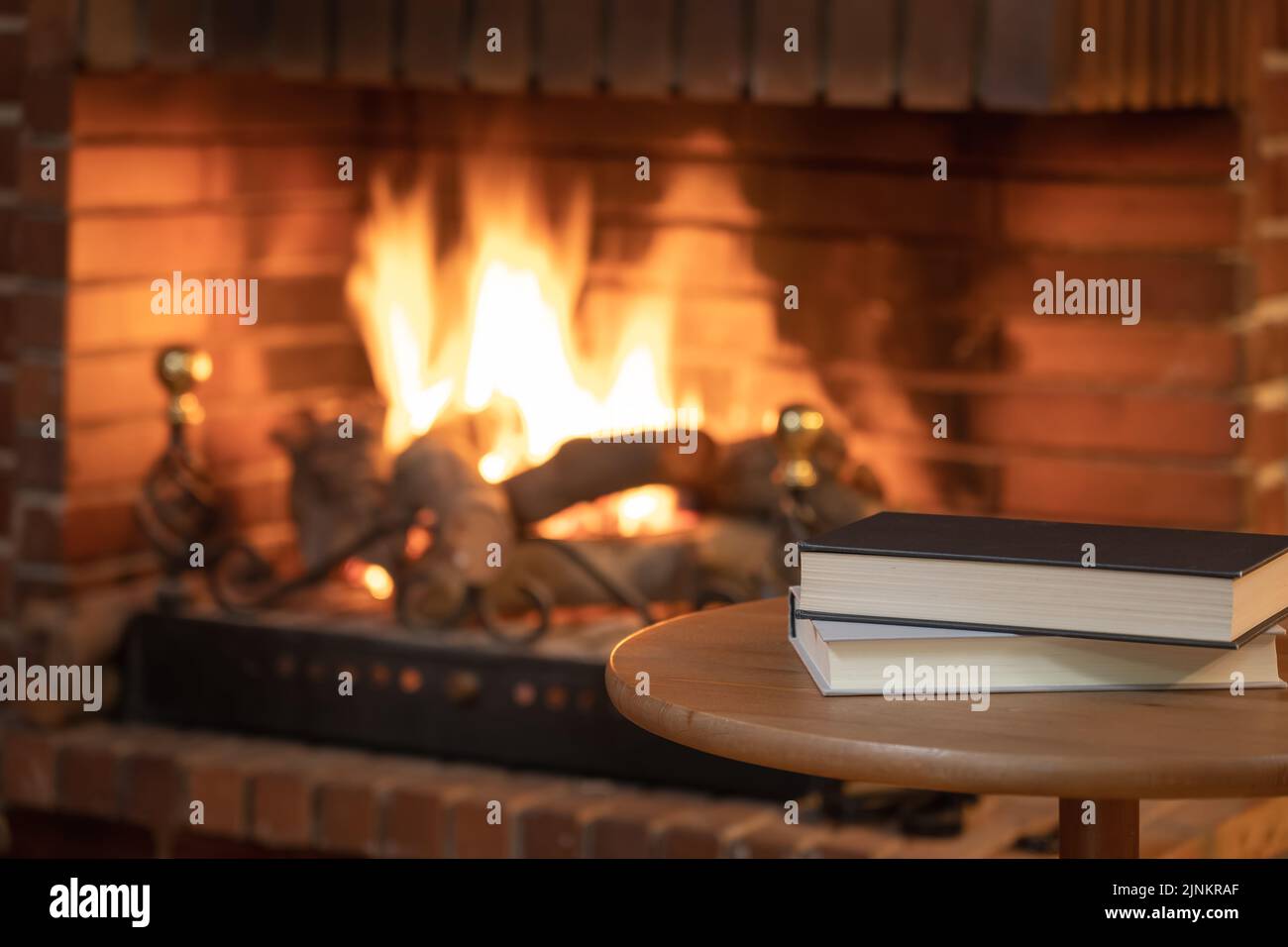 Livres empilés sur une petite table devant une cheminée avec feu en hiver. Banque D'Images
