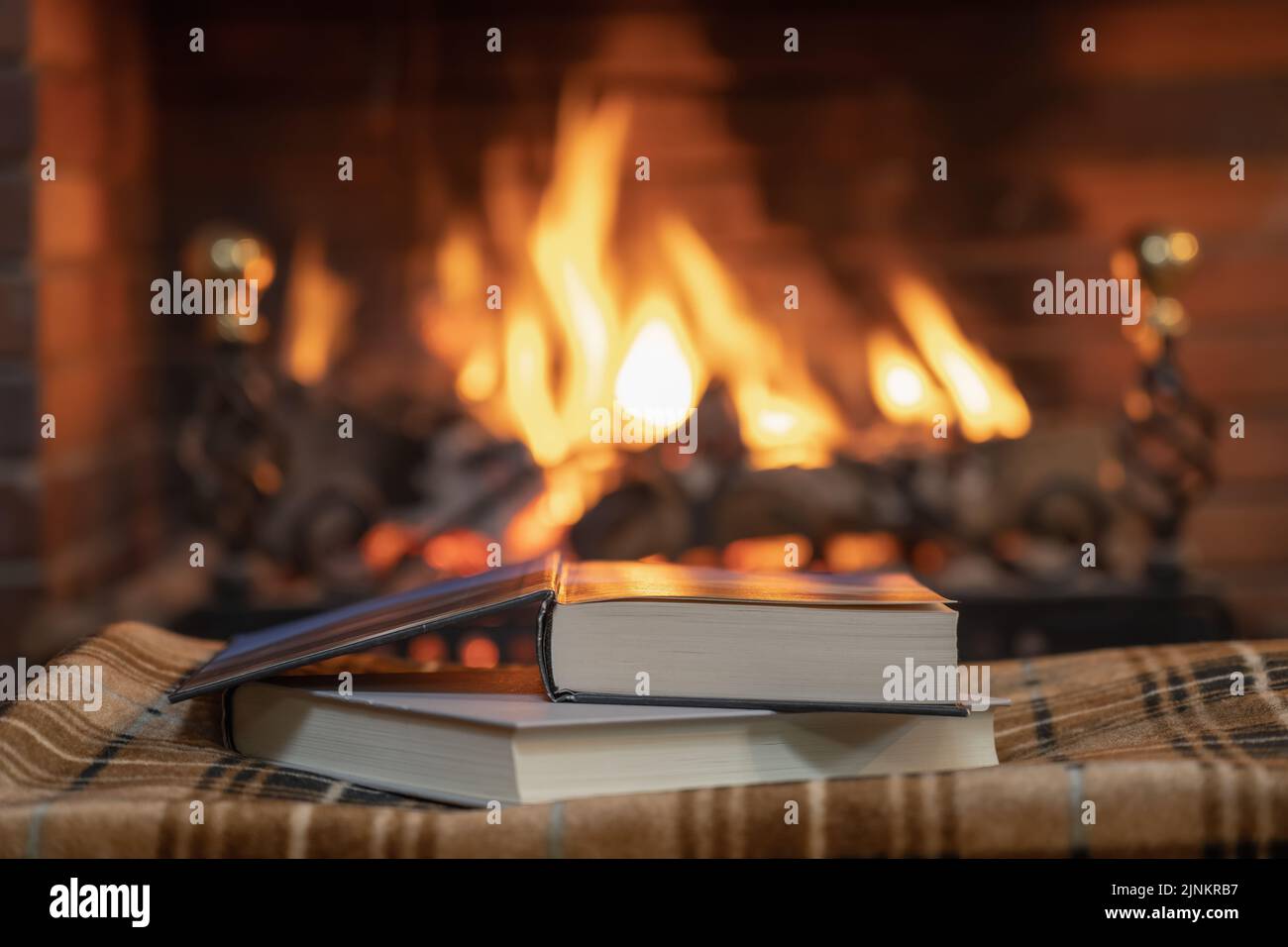 Livres empilés sur une couverture confortable devant une cheminée avec cheminée Banque D'Images