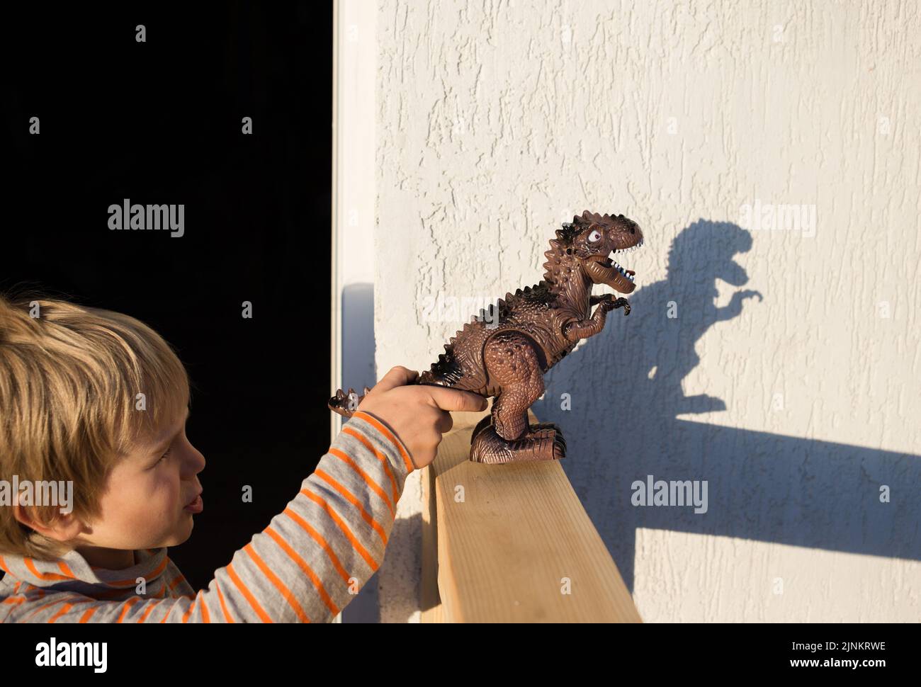 garçon joue avec un jouet de dinosaure, faisant des ombres contrastées intéressantes de lui sur un mur léger. Beau jour ensoleillé. Bonne enfance, idées de jeux Banque D'Images