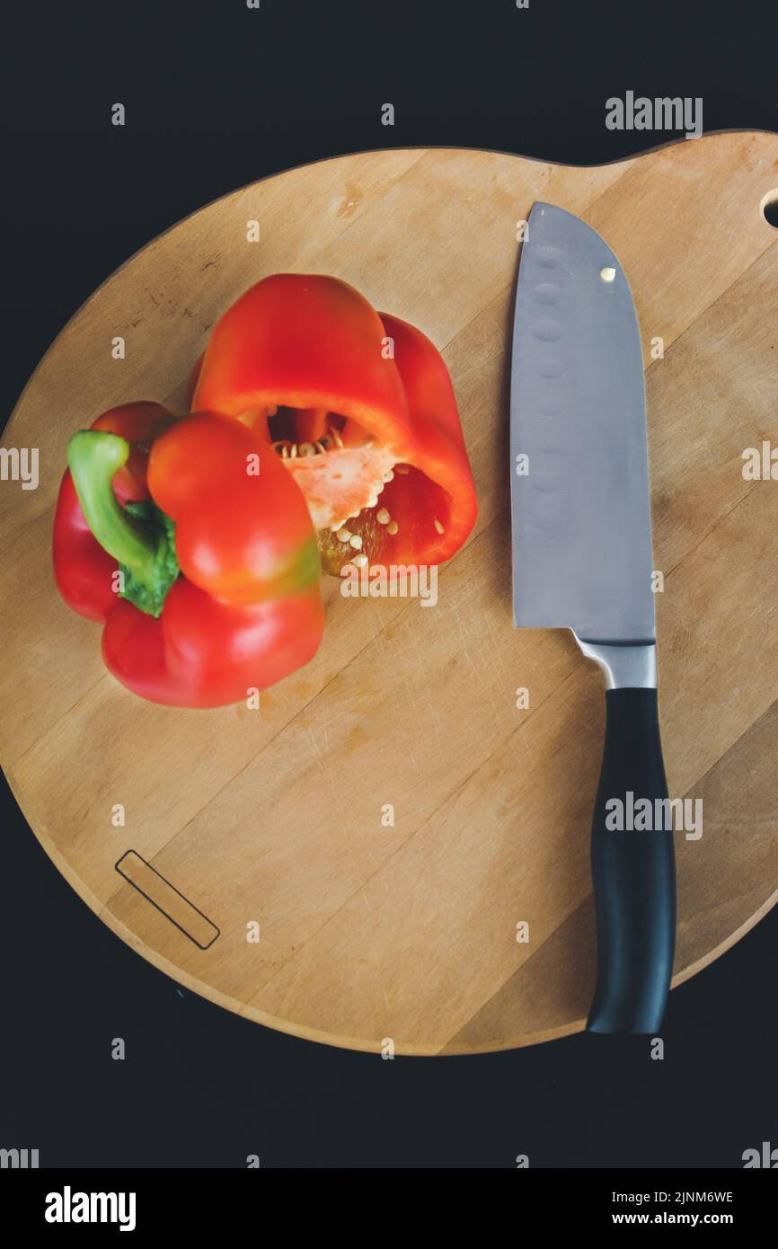 Un gros couteau de cuisine coupe un poivron sur deux parties en gros plan sur une planche en bois. Banque D'Images
