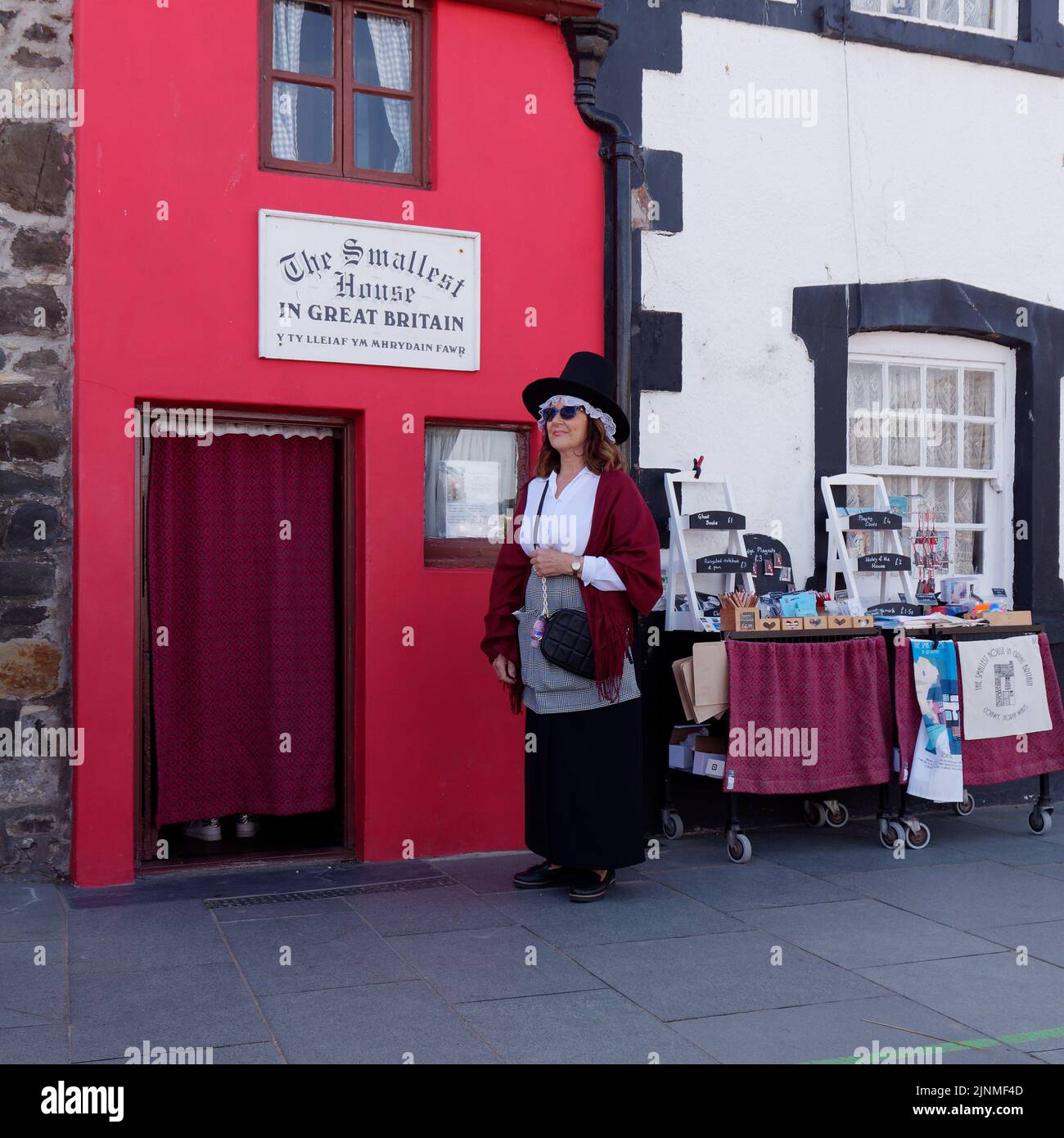 Conwy, Clwyd, pays de Galles, 07 août 2022: La dame dans un chapeau se tient à l'extérieur de la plus petite maison de Grande-Bretagne. Banque D'Images