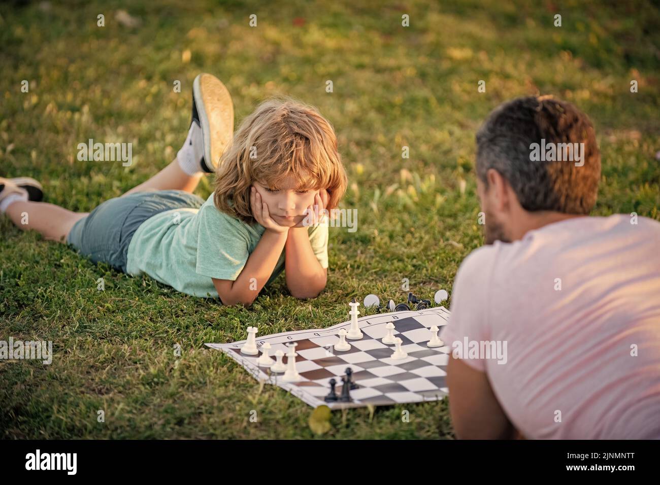 famille heureuse de parents et fils enfant jouant aux échecs sur l'herbe verte dans le parc extérieur, joueurs d'échecs Banque D'Images