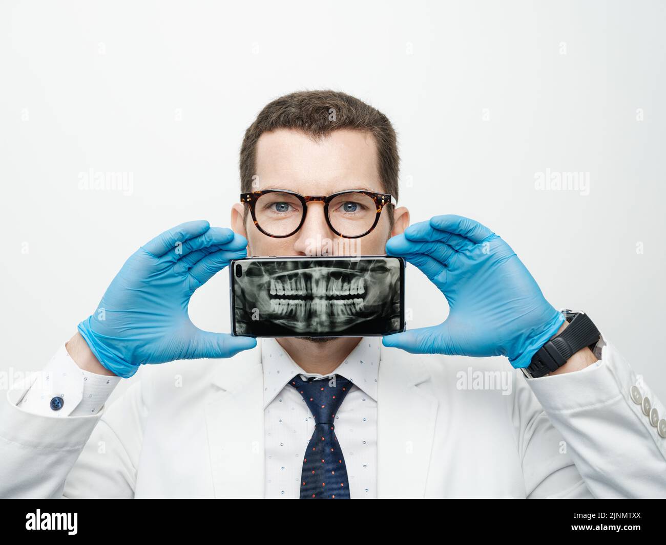Un dentiste masculin recouvre sa bouche avec un smartphone avec des rayons X de ses dents sur un écran d'appareil. Banque D'Images