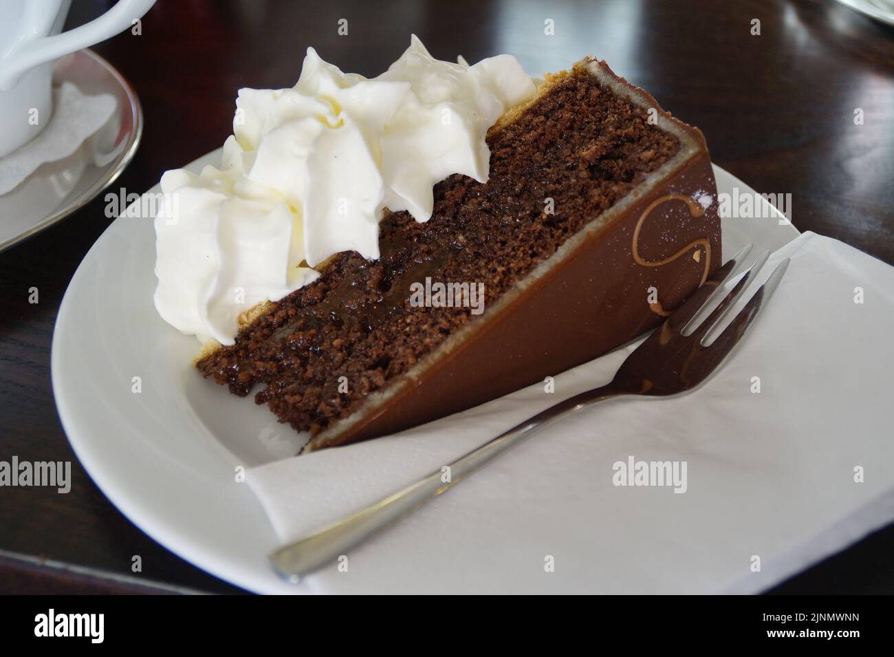 Un délicieux gâteau au chocolat de Vienne ou Sachertorte avec de la crème fouettée et une petite fourchette sur une assiette Banque D'Images