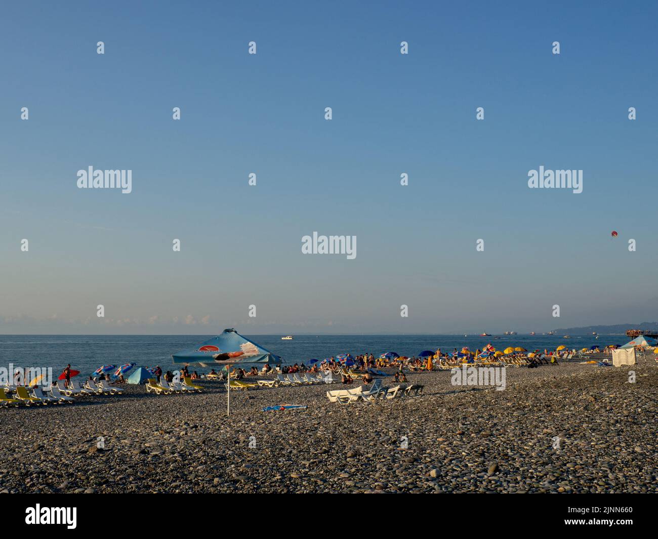 Batumi, Géorgie. 08.02.2022 Plage publique de galets sur la côte de la mer Noire. Beaucoup de gens sur l'eau. Personnes sur des chaises longues et sous des parasols. Chaud e Banque D'Images