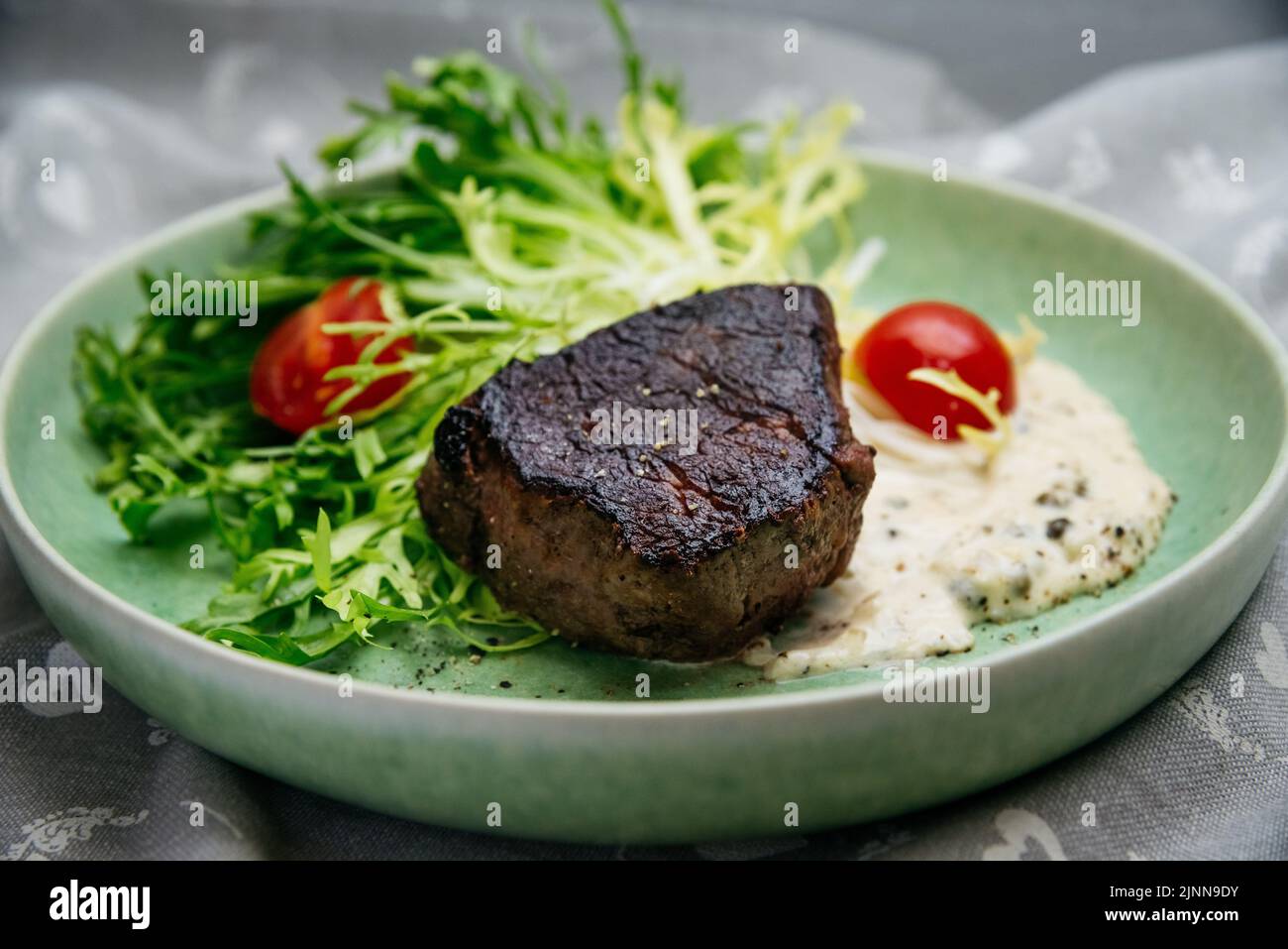 Erreur culinaire. Un morceau de viande de bœuf surcuite et brûlée sur des feuilles de salade avec des tomates cerises et de la sauce blanche, sur une assiette verte. Banque D'Images