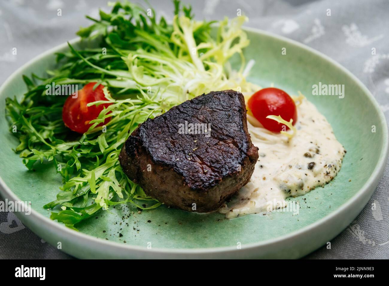 Erreur culinaire. Un morceau de viande de bœuf surcuite et brûlée sur des feuilles de salade avec des tomates cerises et de la sauce blanche, sur une assiette verte. Banque D'Images