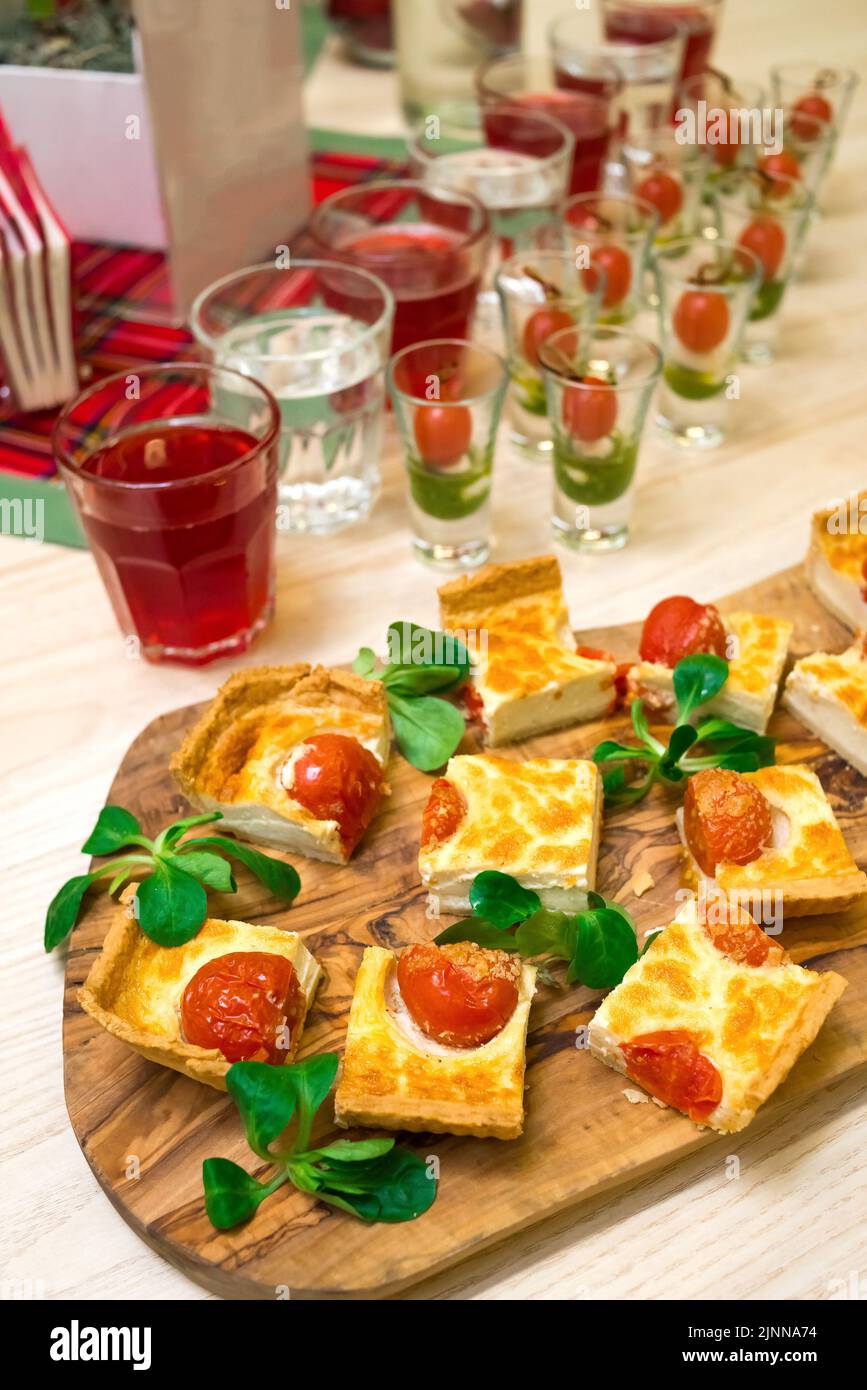 tranches carrées de quiche avec tomates cerises et feuilles de laitue de maïs sur une planche à découper en bois, table de hors-d'œuvre avec en-cas et canapés Banque D'Images