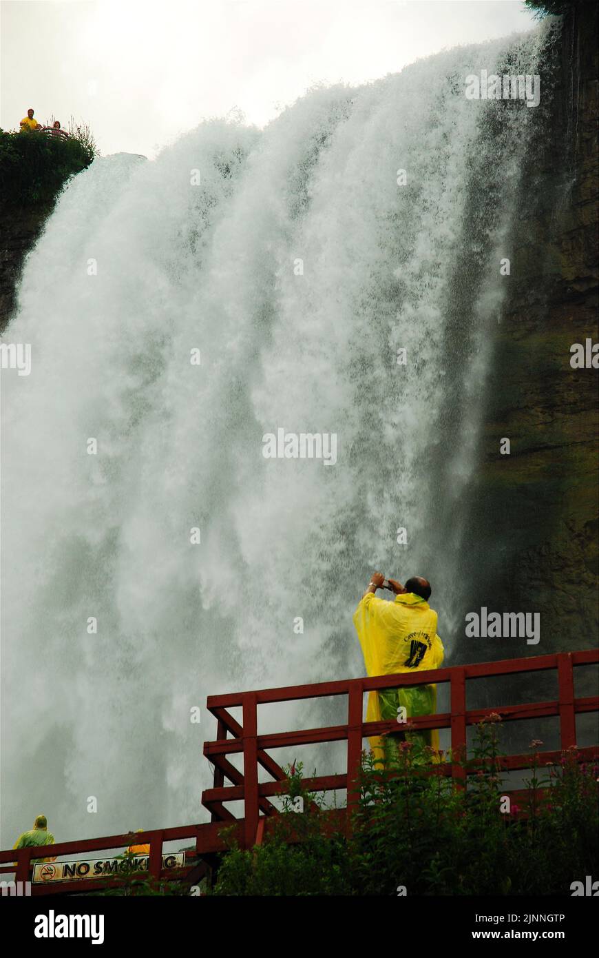 Deux visiteurs à ponchos jaunes prennent la vue de la puissance des chutes du Niagara depuis la base pendant la visite de la grotte des vents Banque D'Images