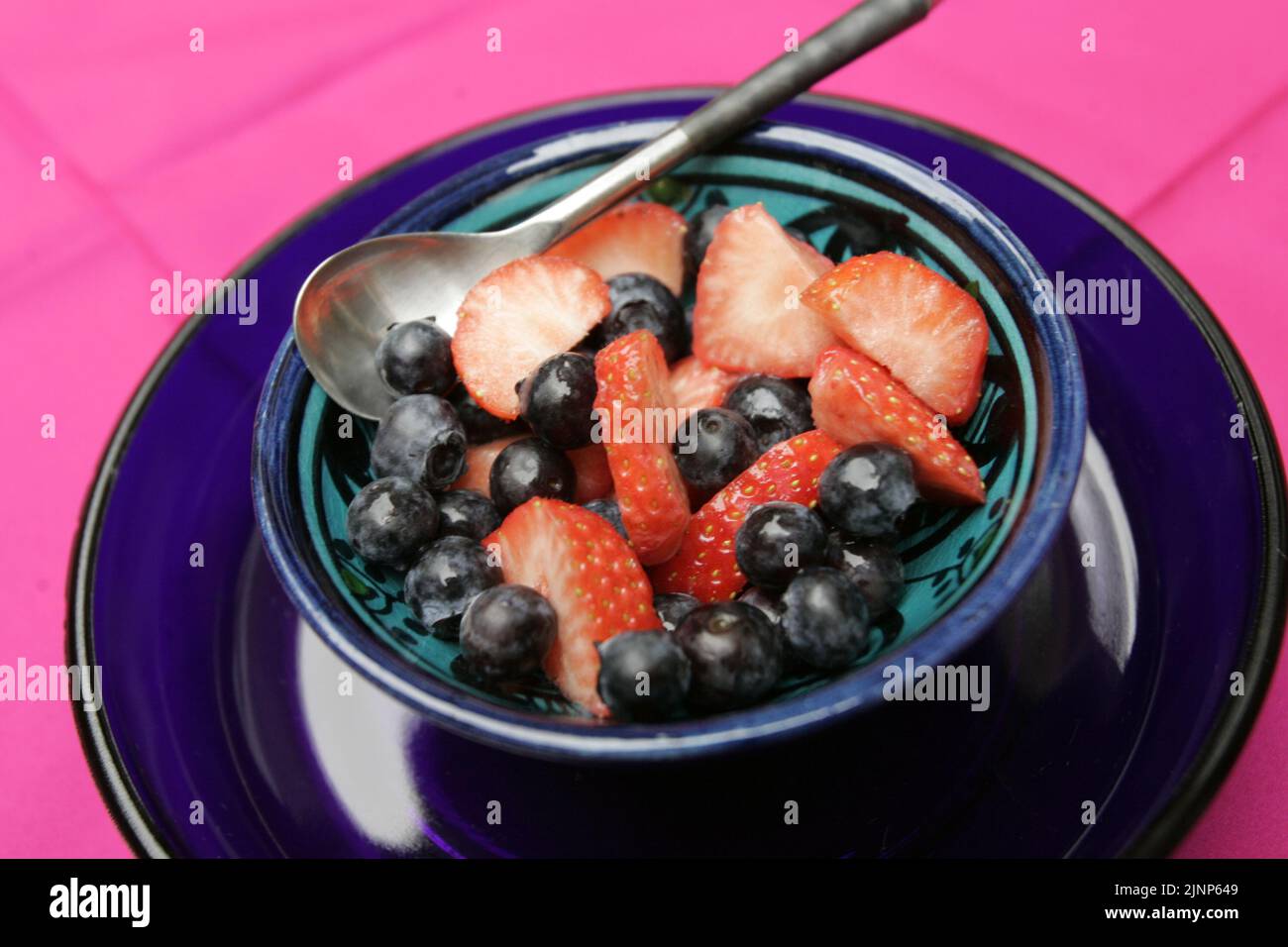 Un bol de fruits de petit déjeuner sain de bleuets et de fraises, sur une assiette en verre bleu Banque D'Images