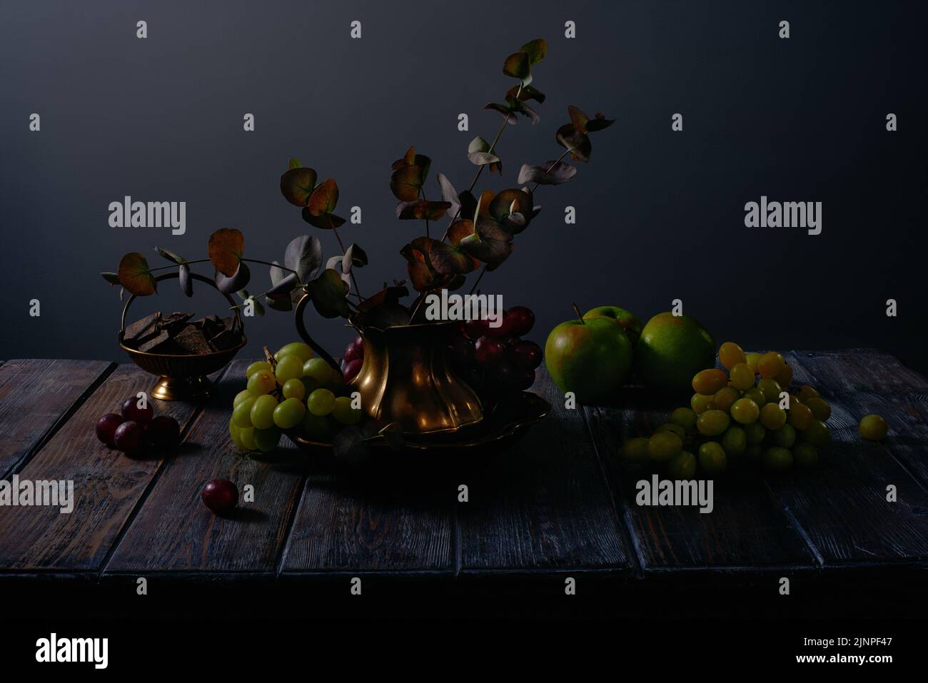 Les fruits continuent à vivre avec des raisins, des pommes, du chocolat et des ustensiles anciens en cuivre sur fond de table en bois foncé Banque D'Images