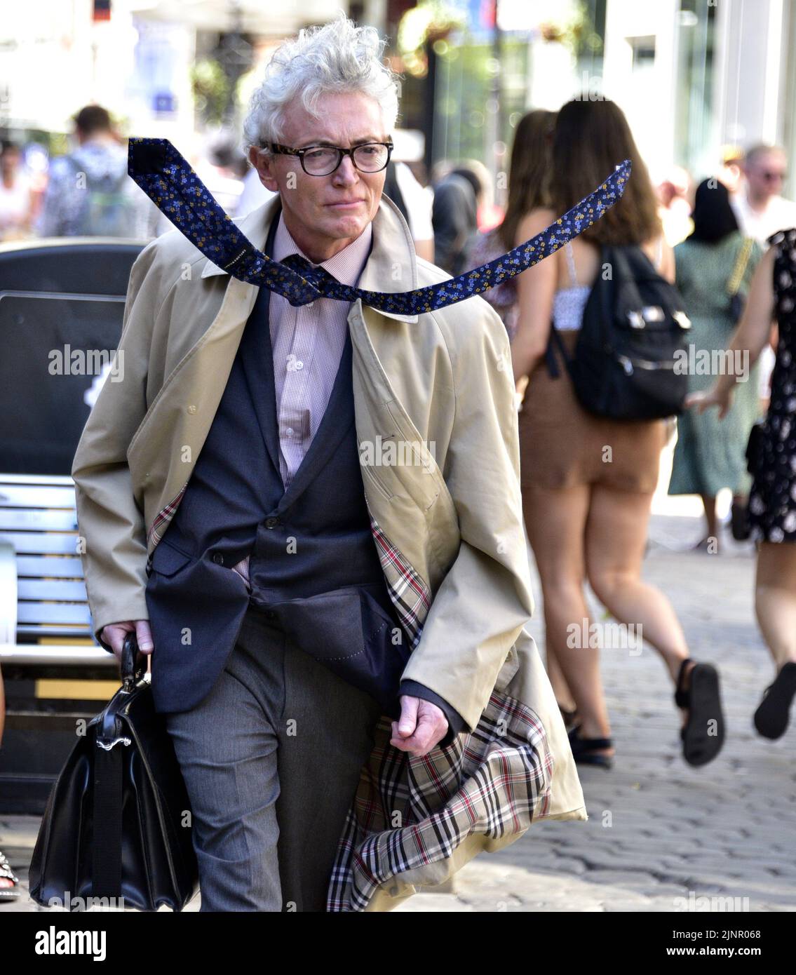 Un homme plus âgé, portant un manteau et un gilet, avec une cravate qui tourne à un angle inhabituel, pose pour attendre des dons dans le centre de Manchester, Royaume-Uni, îles britanniques. Banque D'Images