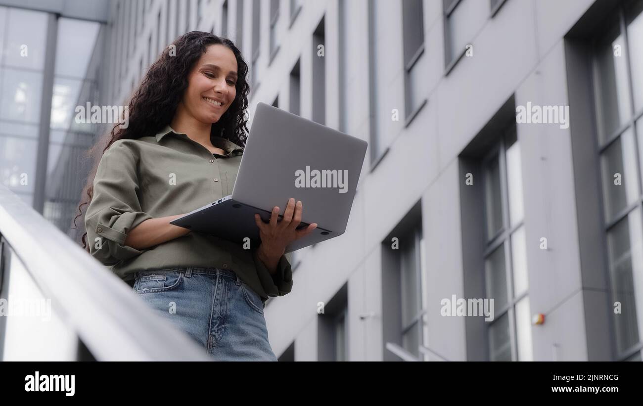 Une femme d'affaires réussie de 30s travaillant à taper sur un ordinateur portable en utilisant le Wi-Fi gratuit de la ville bavardant sur un ordinateur sans fil se tenant près du bâtiment de l'entreprise de bureau femme Banque D'Images