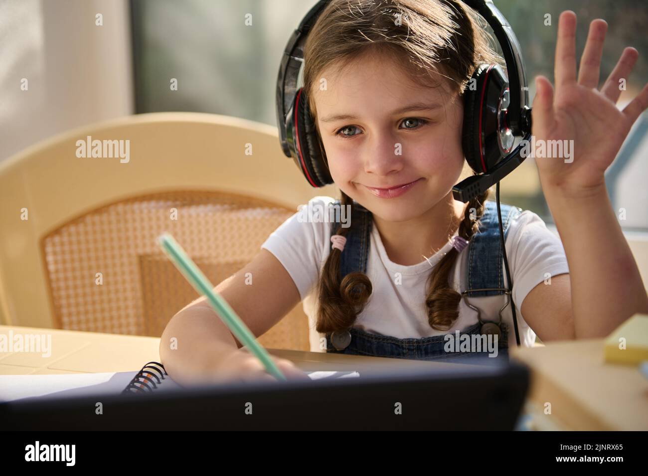 Gros plan d'un élève du primaire intelligent, portant un casque audio, souriant tout en regardant une leçon vidéo en ligne Banque D'Images