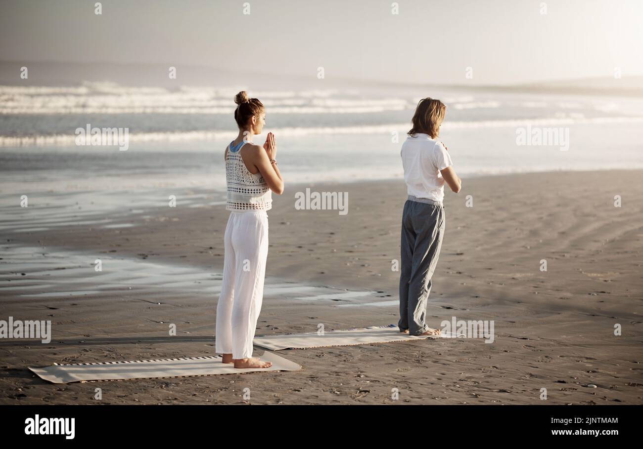 Le cadre idéal pour un calme parfait. Un jeune couple pratiquant le yoga ensemble sur la plage. Banque D'Images