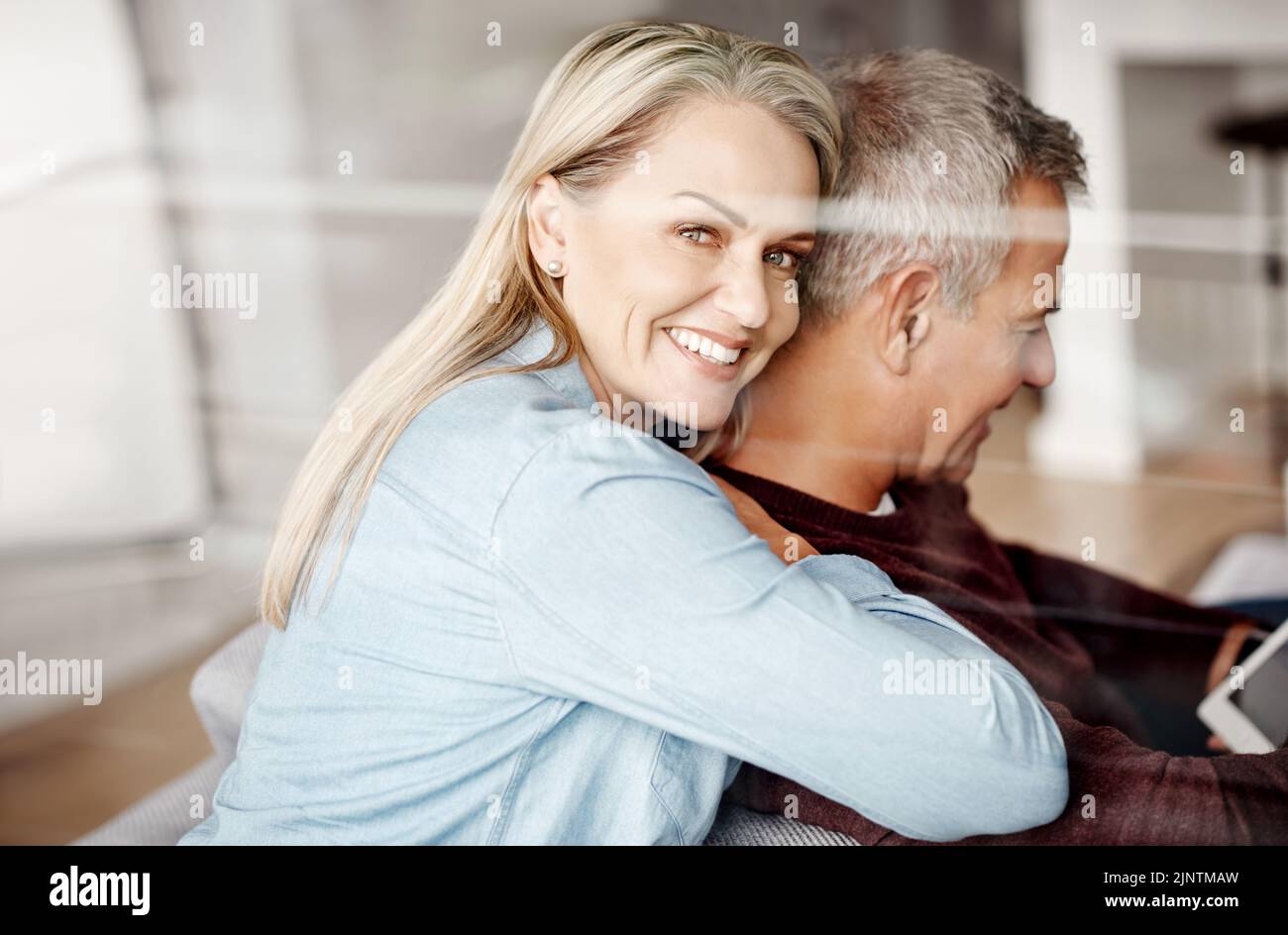 Quand vous trouvez votre roi se tenir sur lui. Une femme mûre embrassant son mari pendant qu'il utilise une tablette numérique sur le canapé à la maison. Banque D'Images