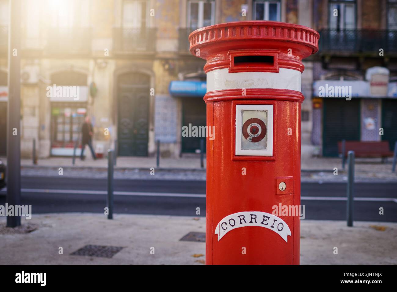 Il est à votre disposition si vous voulez envoyer une lettre. Une boîte aux lettres rouge debout tout seul dans la ville dehors pendant la journée. Banque D'Images