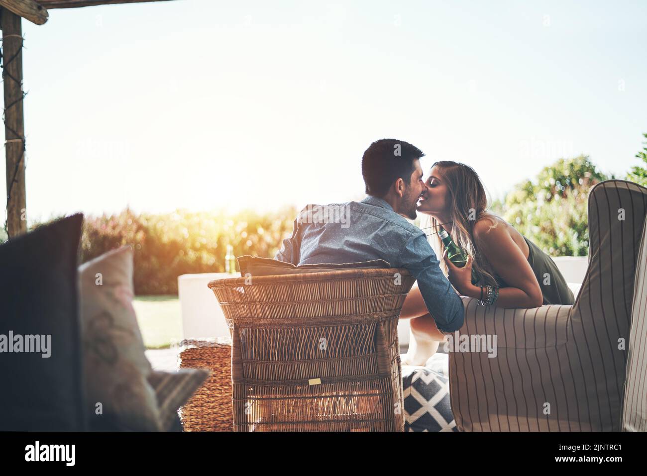 Les meilleurs sièges de la maison. Photo d'un jeune couple affectueux qui embrasse tout en dégustant des bières sur leur patio. Banque D'Images