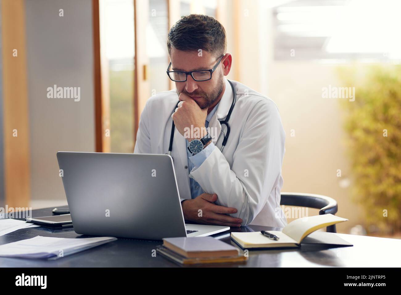 Les dossiers médicaux sont la clé d'une bonne santé. Un beau médecin masculin travaillant sur son ordinateur portable tout en étant assis dans son bureau. Banque D'Images