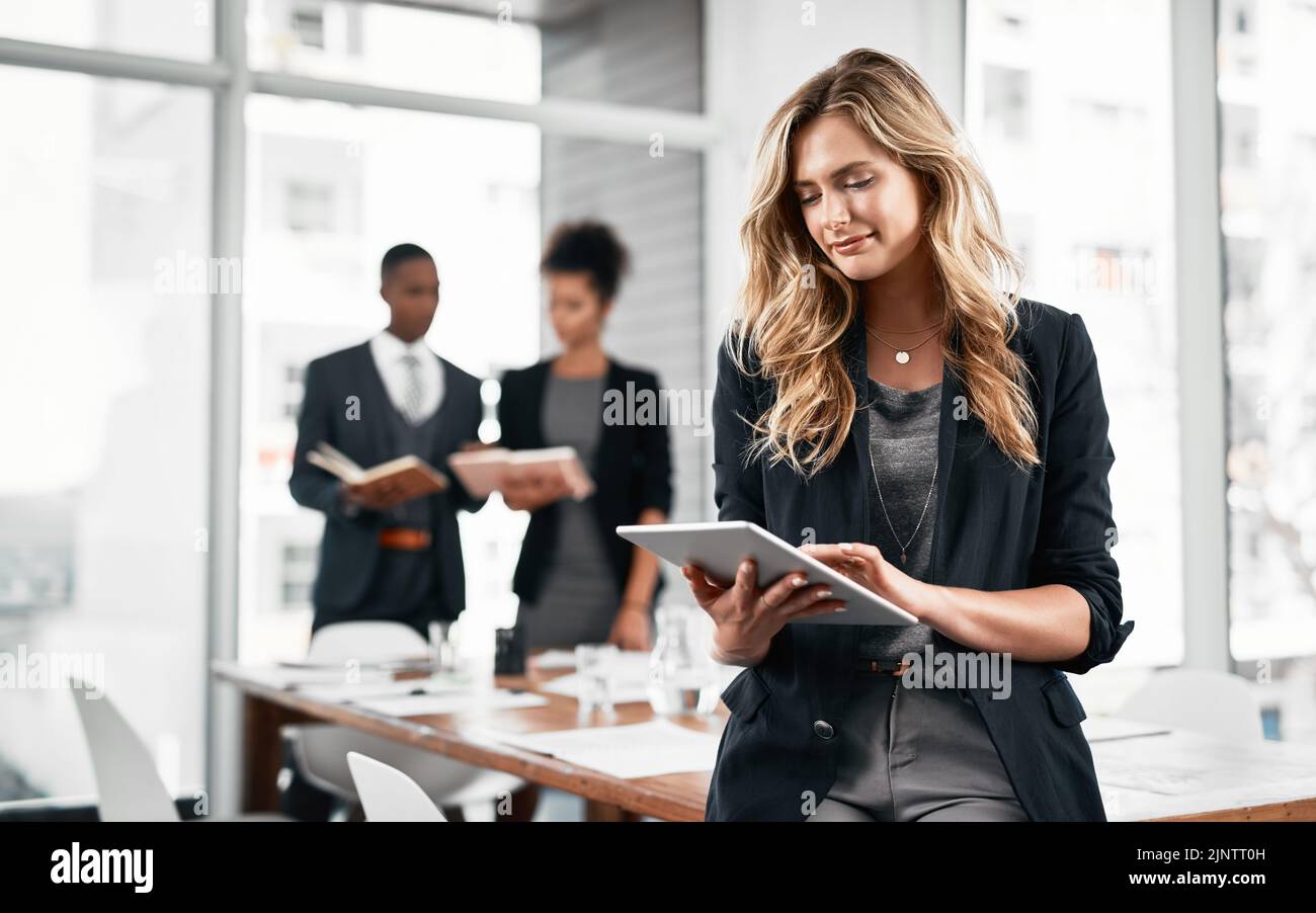 Il y a tant de découvertes innovantes en ligne : une jeune femme d'affaires utilisant une tablette numérique dans un bureau avec ses collègues en arrière-plan. Banque D'Images