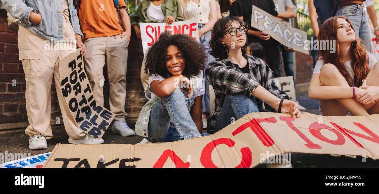 Adolescente souriante à la caméra tout en étant assise avec un groupe de jeunes militants pour la paix. Jeunes multiethniques affichant des affiches et banne Banque D'Images