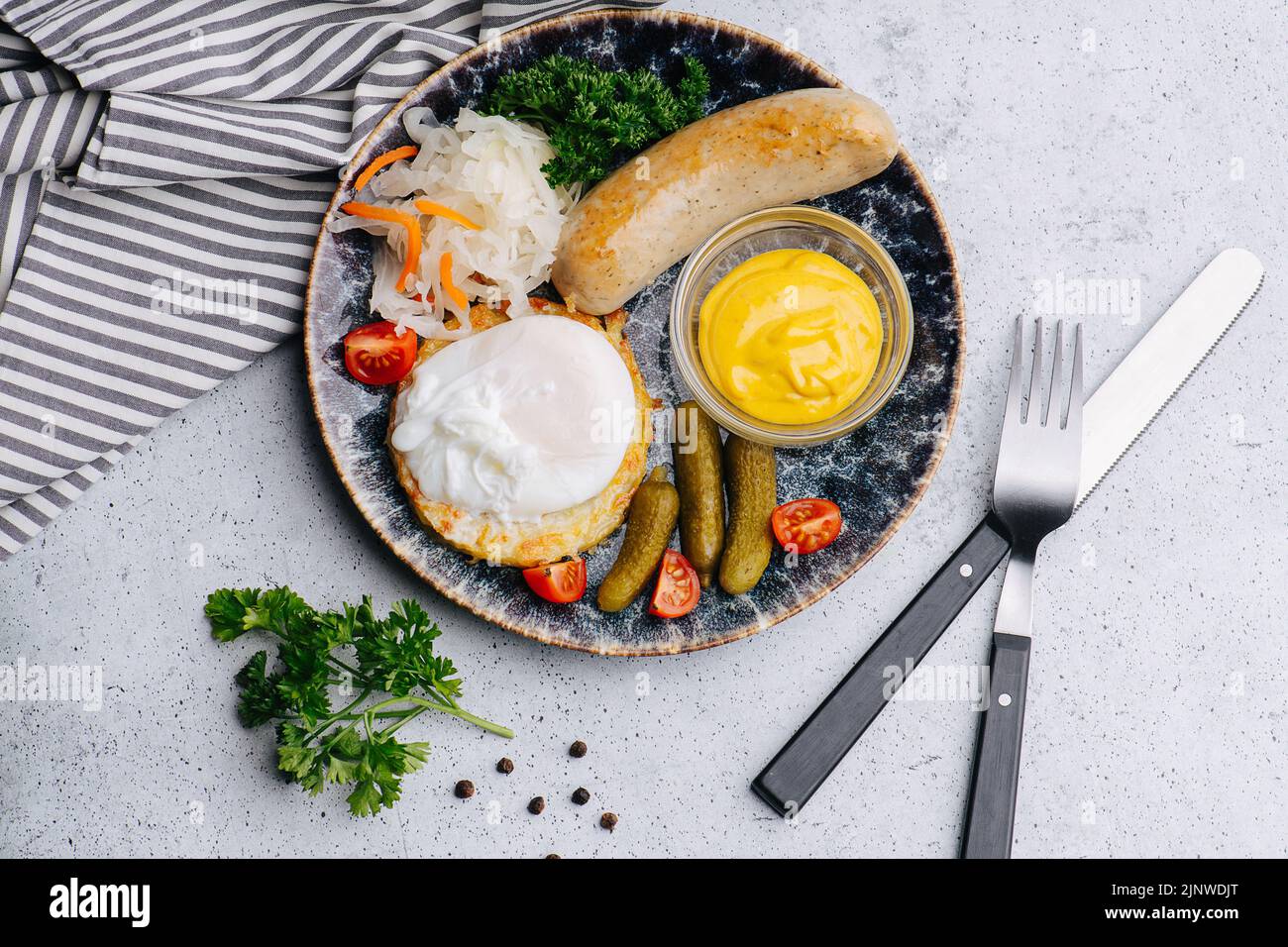 Petit déjeuner copieux avec saucisse, moutarde, tomates, cornichons sur une assiette sur une serviette à motifs noirs. Vue de dessus. Banque D'Images