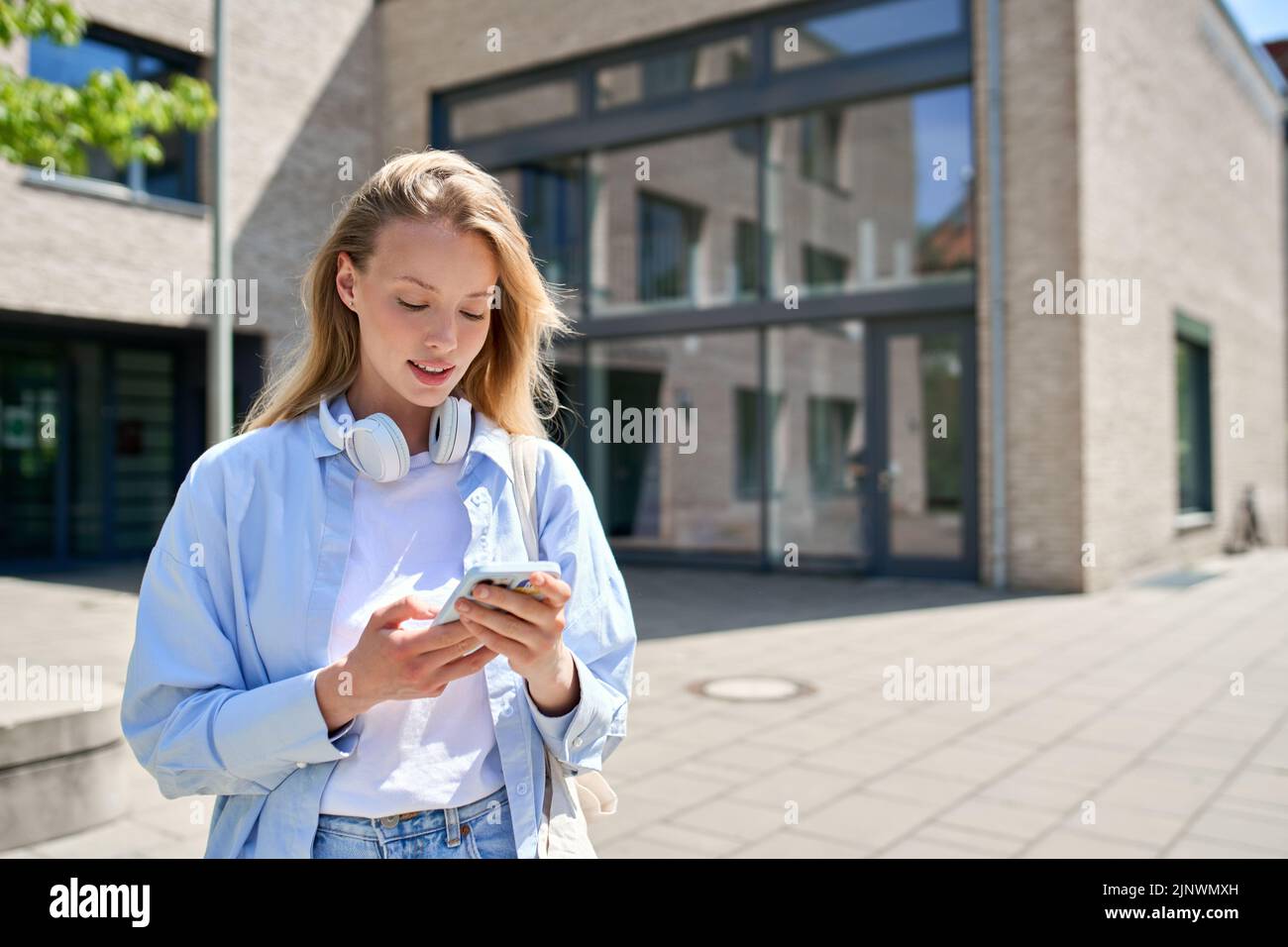 Belle fille étudiante à l'université en utilisant un smartphone debout à l'extérieur. Banque D'Images