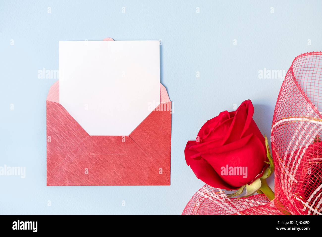 Vue de dessus de l'enveloppe rouge et carte blanche vide avec belle rose sur fond bleu clair, espace de copie Banque D'Images