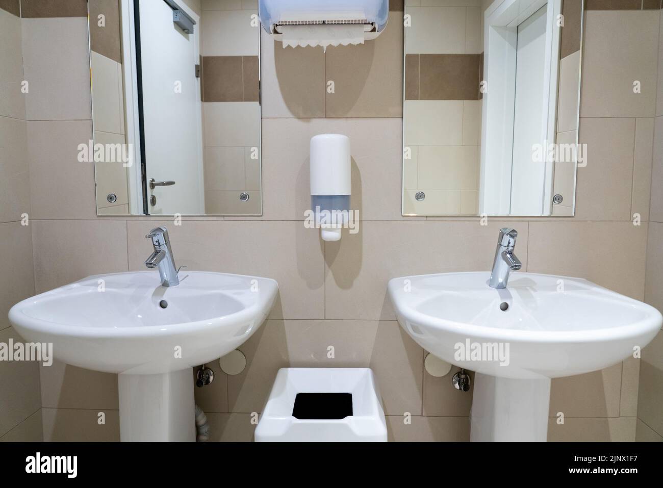 Deux lavabos symétriques dans une toilette publique moderne avec serviettes en papier et vaisselle à savon Banque D'Images