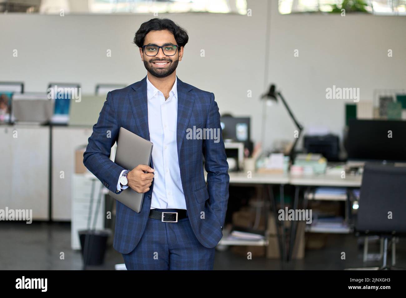 Jeune homme d'affaires indien souriant portant un costume debout au bureau, portrait. Banque D'Images