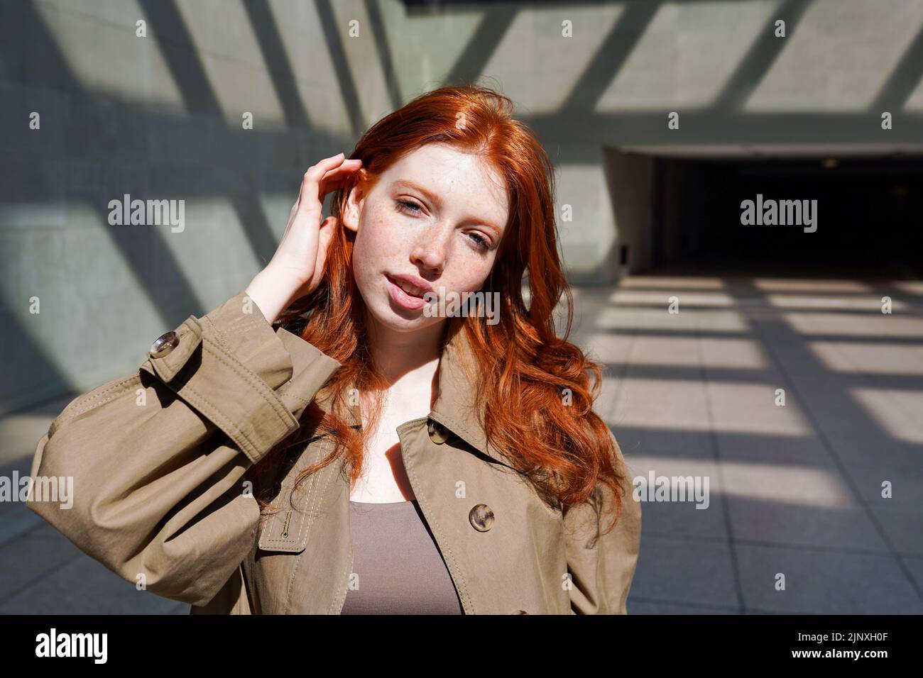 Adolescente à tête rouge regardant un appareil photo debout au milieu des murs urbains. Banque D'Images