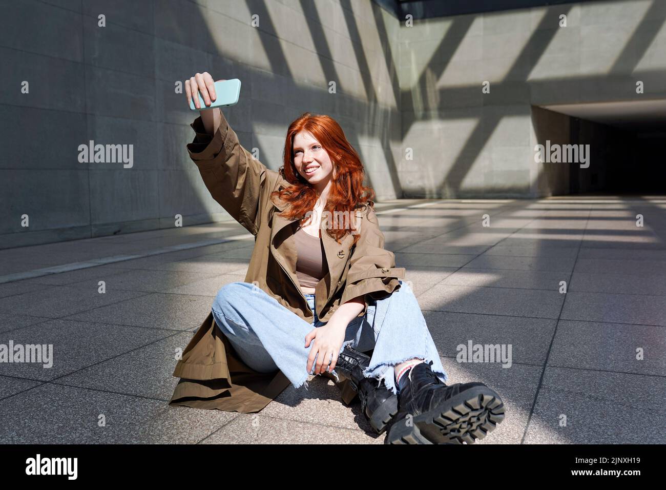 Heureux redhead jeune fille prenant selfie sur le téléphone sur fond urbain murs de ville. Banque D'Images