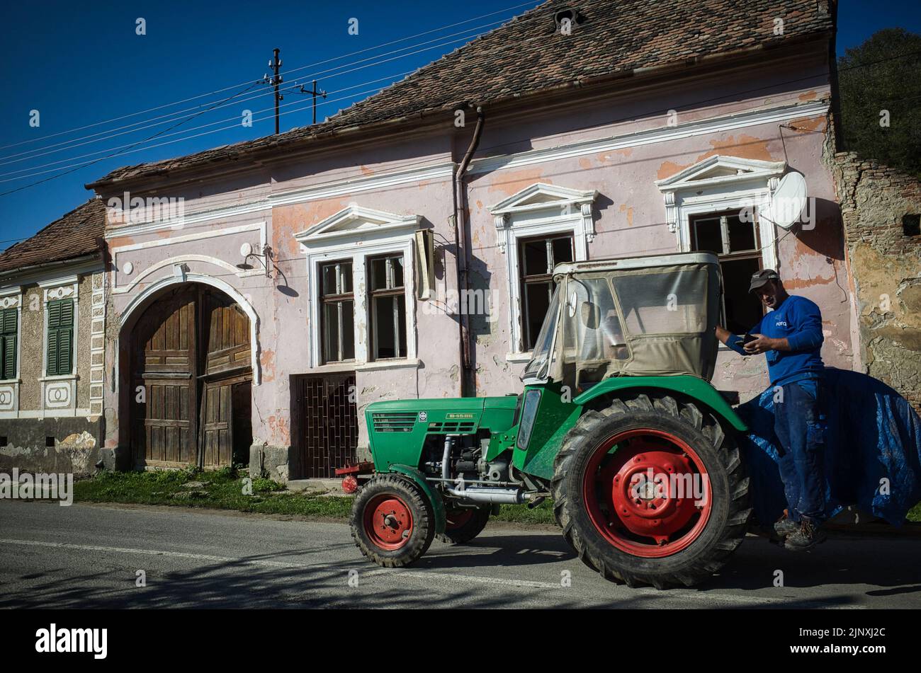 Homme en costume bleu de chaudière envoyant un message texte alors qu'il prend un trajet à la maison sur l'arrière d'un tracteur en Transylvanie Banque D'Images