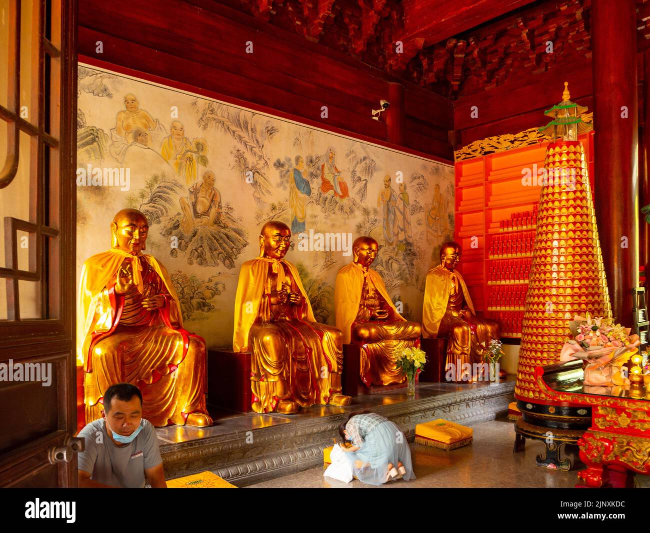 Une femme prie une sculpture ou une statue dorée à l'intérieur d'un temple. La religion traditionnelle chinoise est montrée dans la scène. Banque D'Images