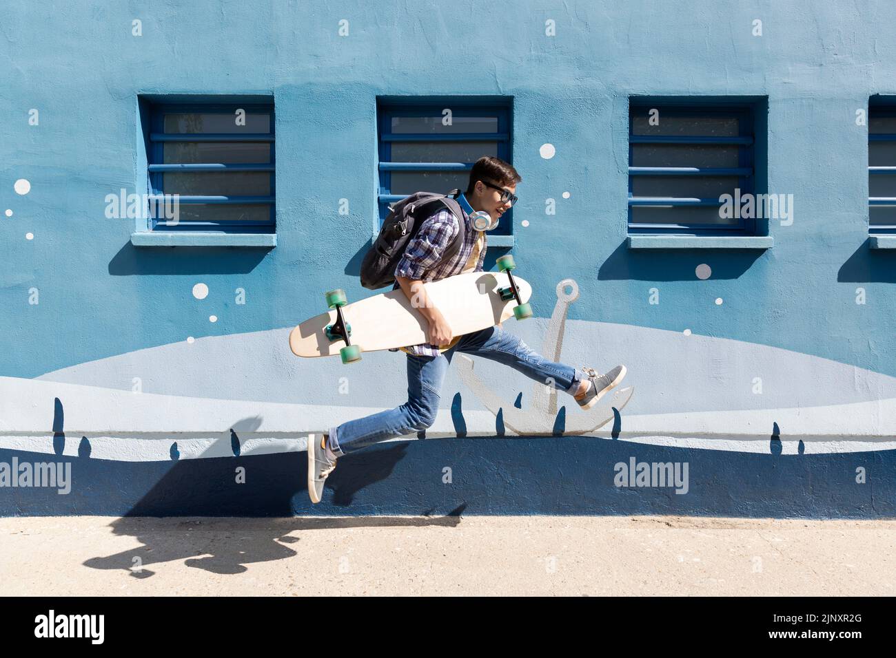Un adolescent de race blanche sautant avec son skateboard à côté d'un mur bleu. Banque D'Images