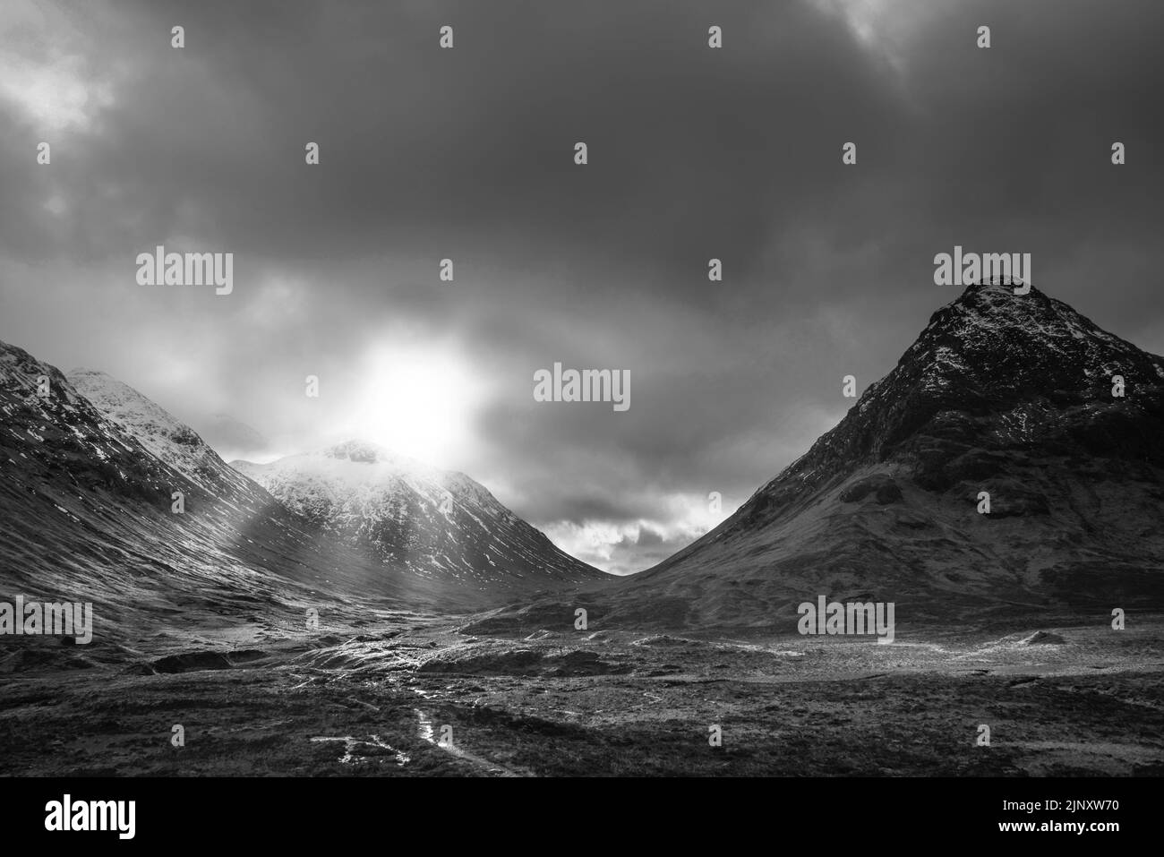 Image de paysage Epic Winter en noir et blanc d'Etive Mor dans les Highlands écossais avec des rayons de soleil coulants entre les sommets Banque D'Images