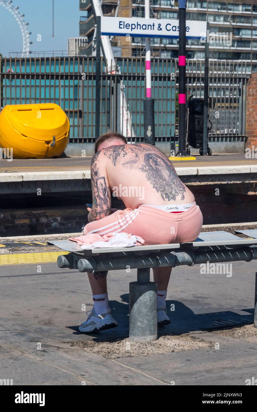 Homme sans chirous avec tatouages assis sur la station Elephant & Castle dans le sud de Londres pendant le temps chaud de la vague de chaleur à l'été 2022. Banque D'Images