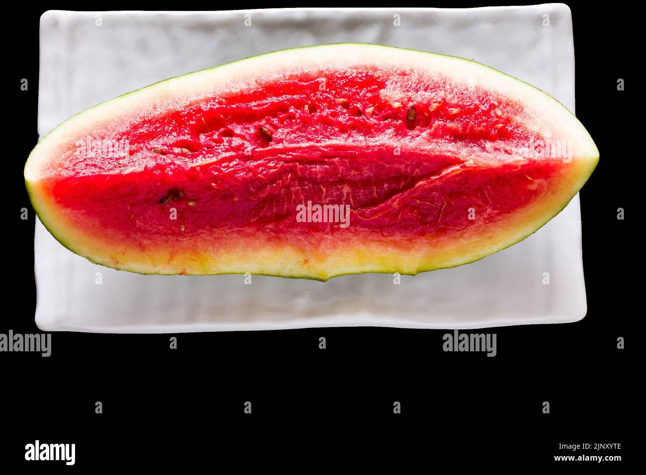 Une seule tranche de fruits frais et doux de pastèque placée sur un plateau blanc et isolée sur fond noir. Vue de dessus, gros plan. Banque D'Images