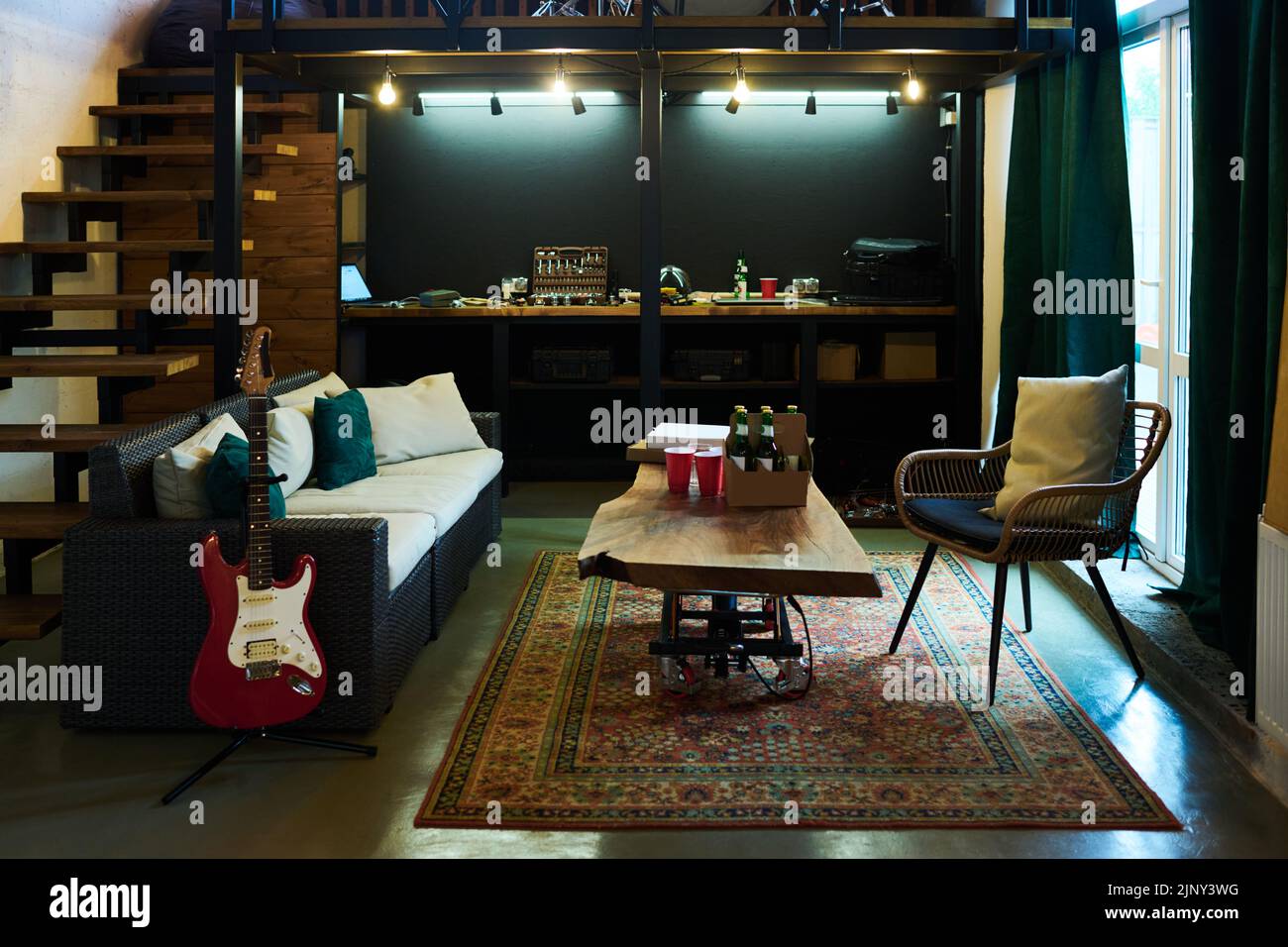 Partie de garage ou chambre à l'intérieur de la maison avec des bouteilles de bière, des tasses et des boîtes carrées sur la table debout entre canapé avec coussins et fauteuil Banque D'Images