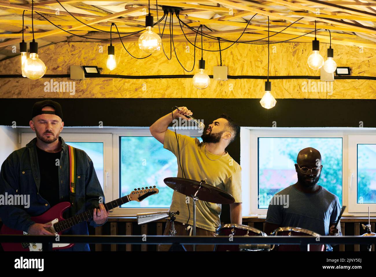 Un jeune chanteur de sexe masculin interprète une chanson en se tenant au milieu d'un guitariste et percussionniste et en tenant le microphone par la bouche Banque D'Images