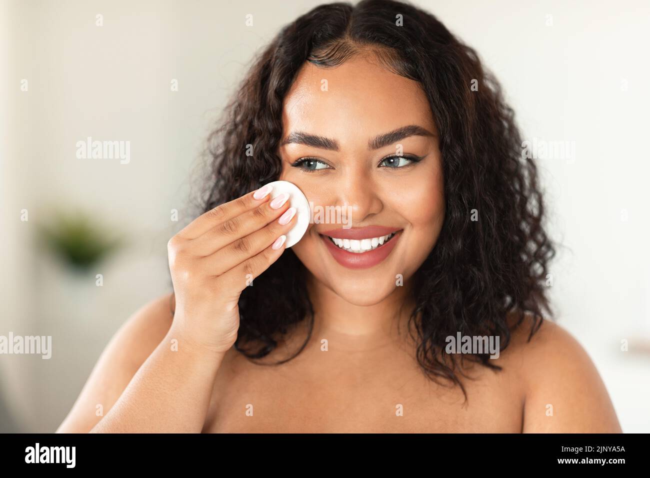 Gros plan portrait d'une femme de taille plus noire utilisant un tampon de coton, gommant la maquillage de son visage, appliquant du toner pour le visage Banque D'Images