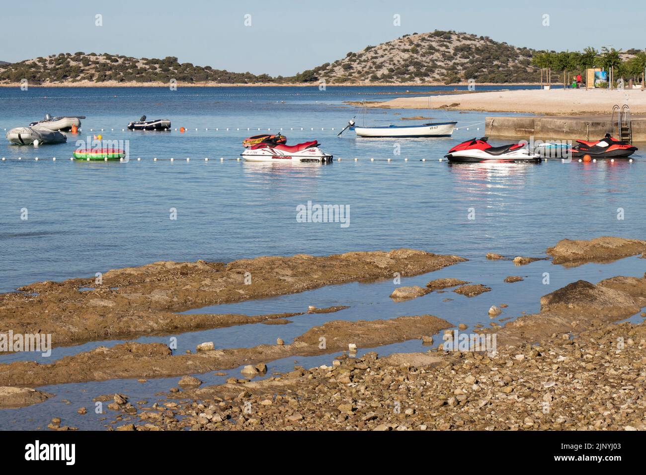 Vodice, Croatie - 13 juillet 2022: Scooter des mers et petits bateaux amarrés par une poire à côté d'une plage vide en Croatie Banque D'Images