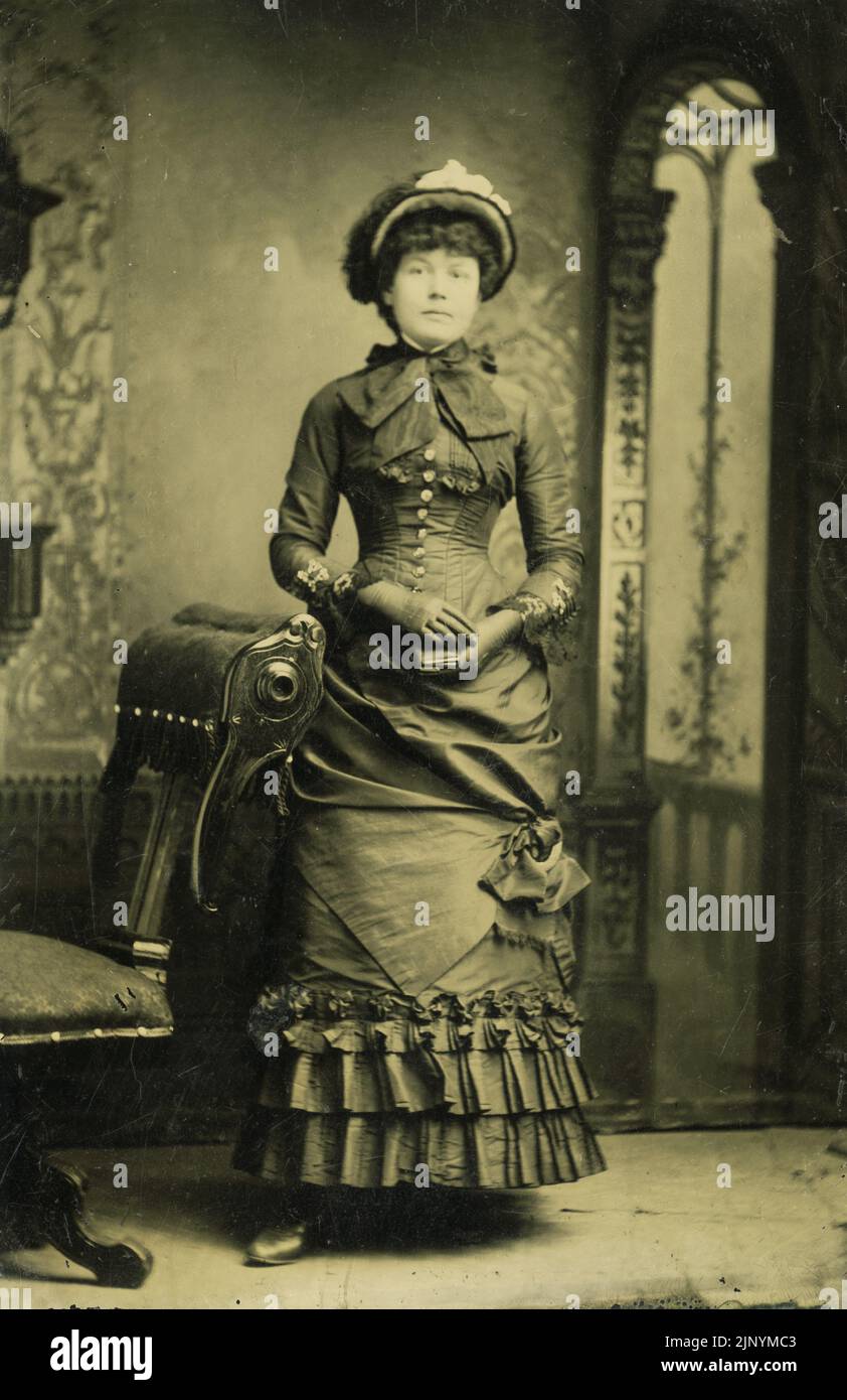 Studio photo fin 19th siècle Portrait d'une femme formelle sérieuse debout dans des vêtements d'époque avec toile de fond vers 1870 - 1880s Banque D'Images