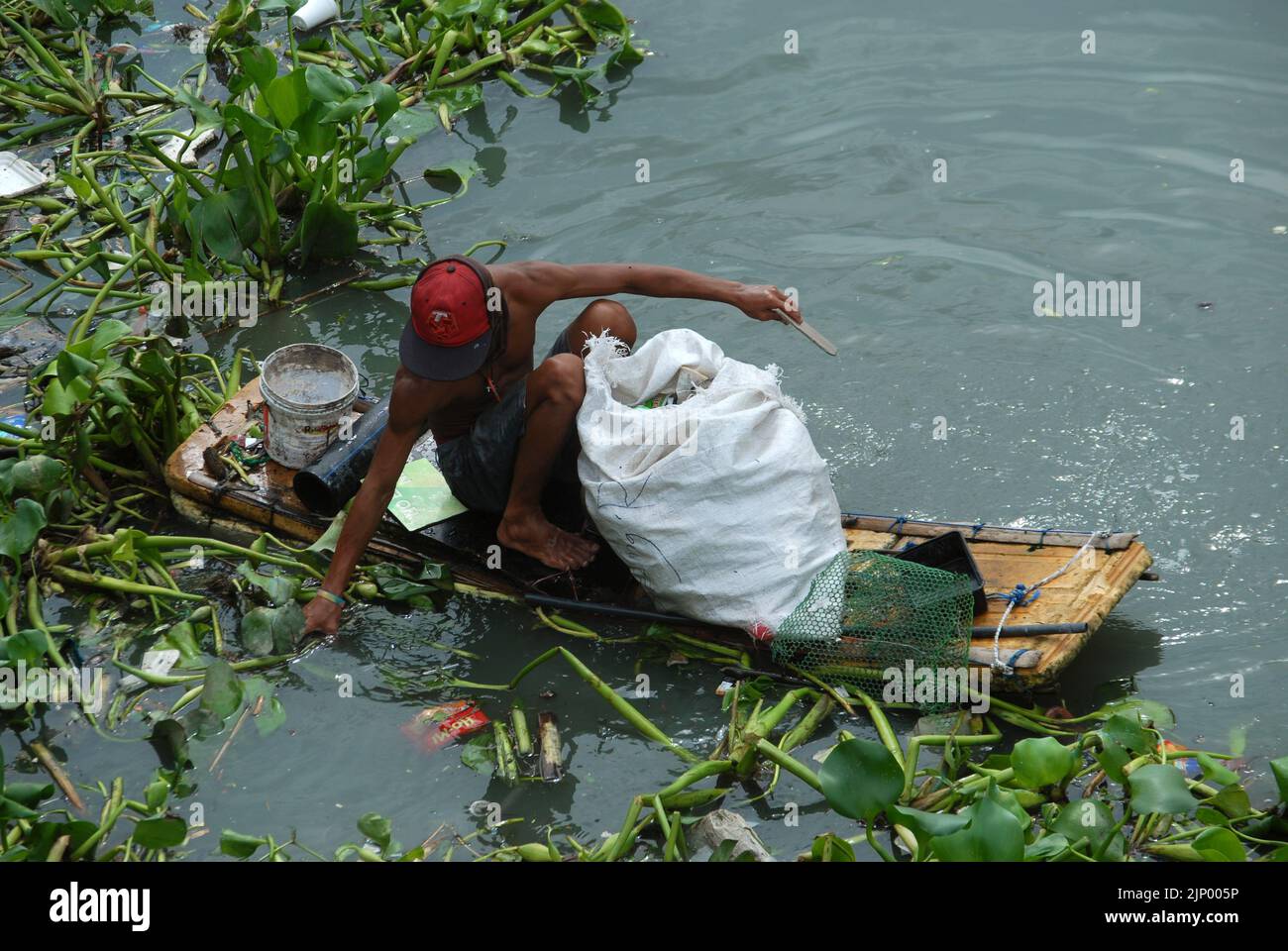 Homme collectant des bouteilles sur un radeau fait maison, Pasig River, Manille. Banque D'Images